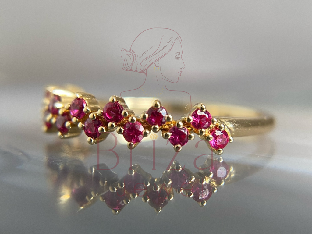 Gold ring with red gemstones on a reflective surface