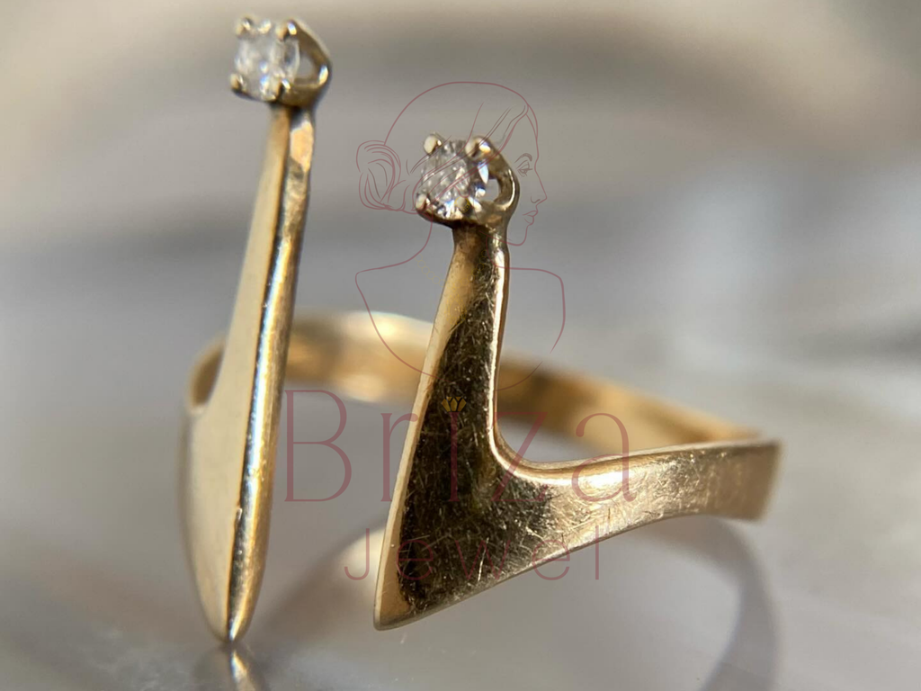 Gold ring with high-heeled shoe design and embedded gemstones on a blurred background.
