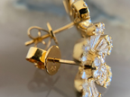 Gold earrings with diamond accents on a reflective surface