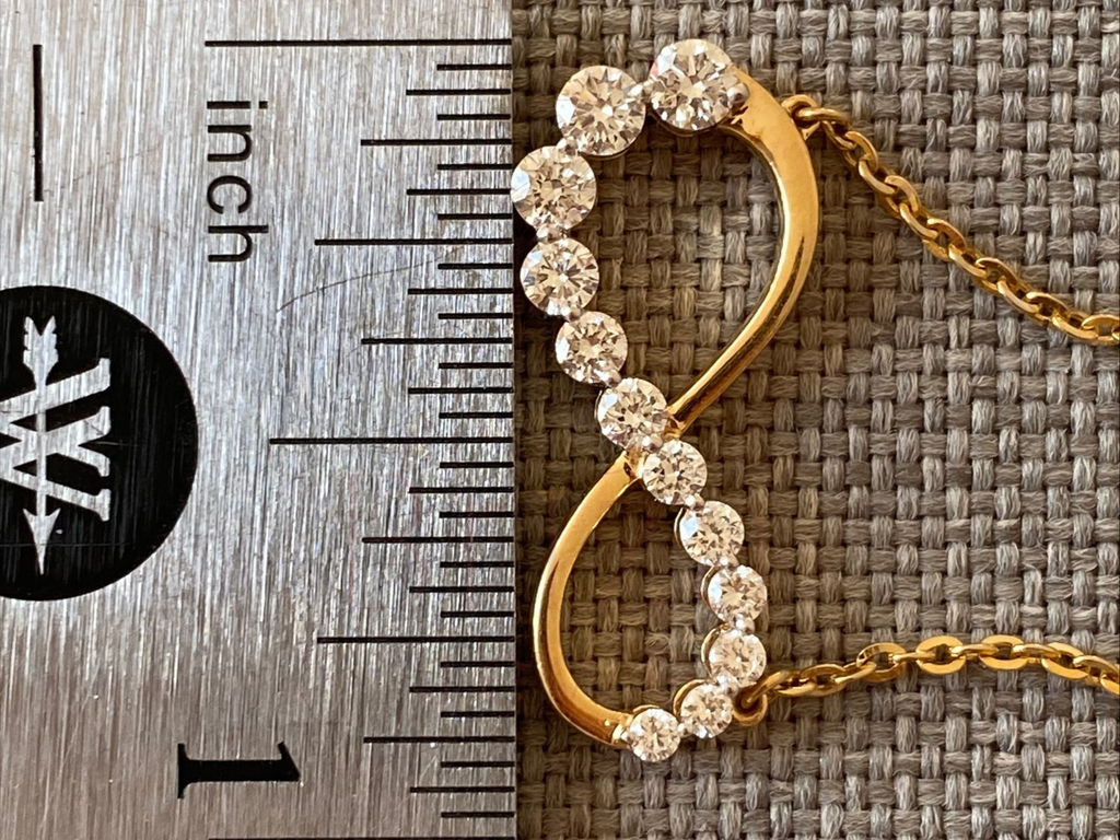 Gold necklace with heart-shaped pendant next to a ruler on a textured surface