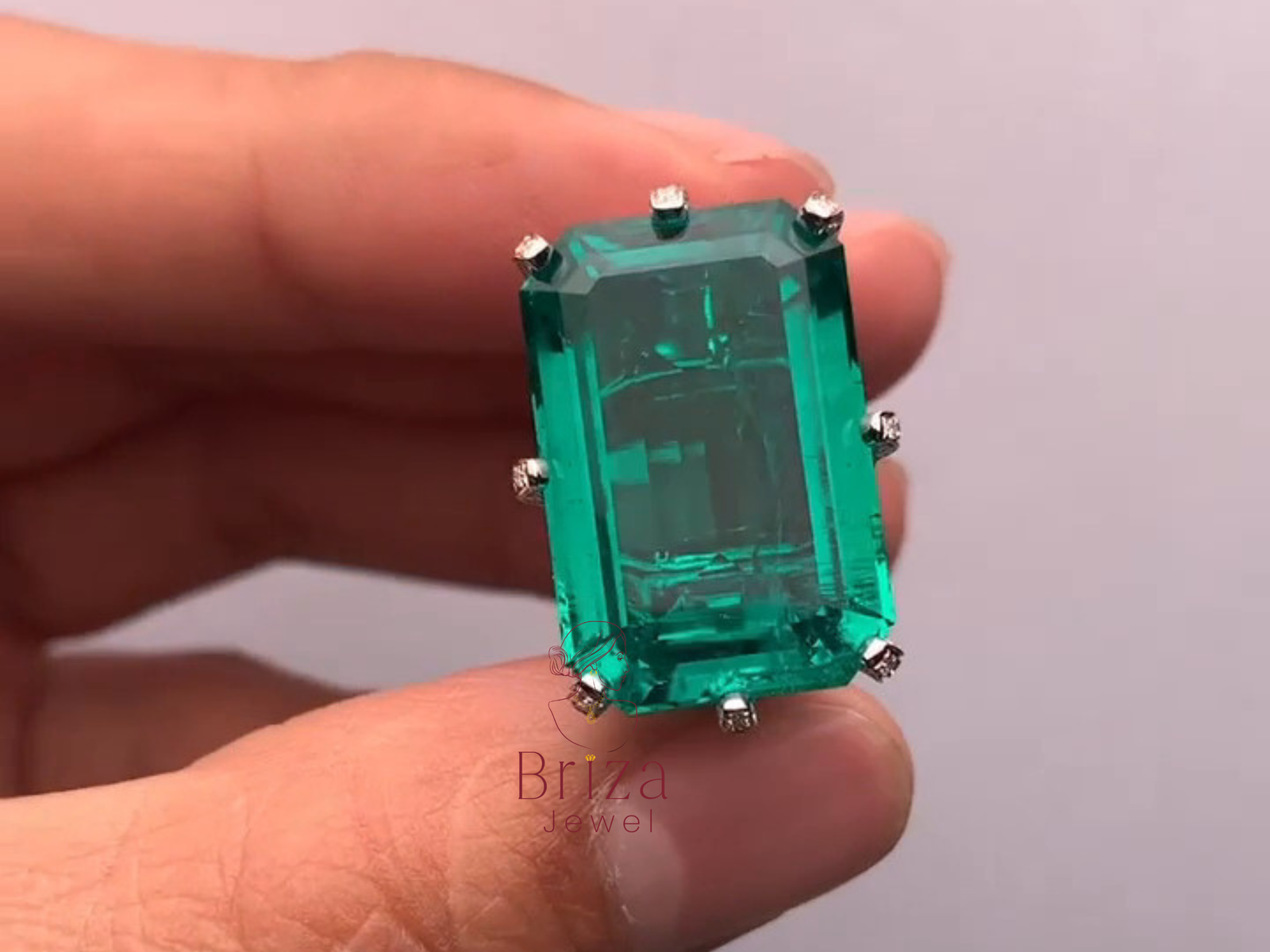 Green emerald gemstone in a silver setting held between fingers against a neutral background