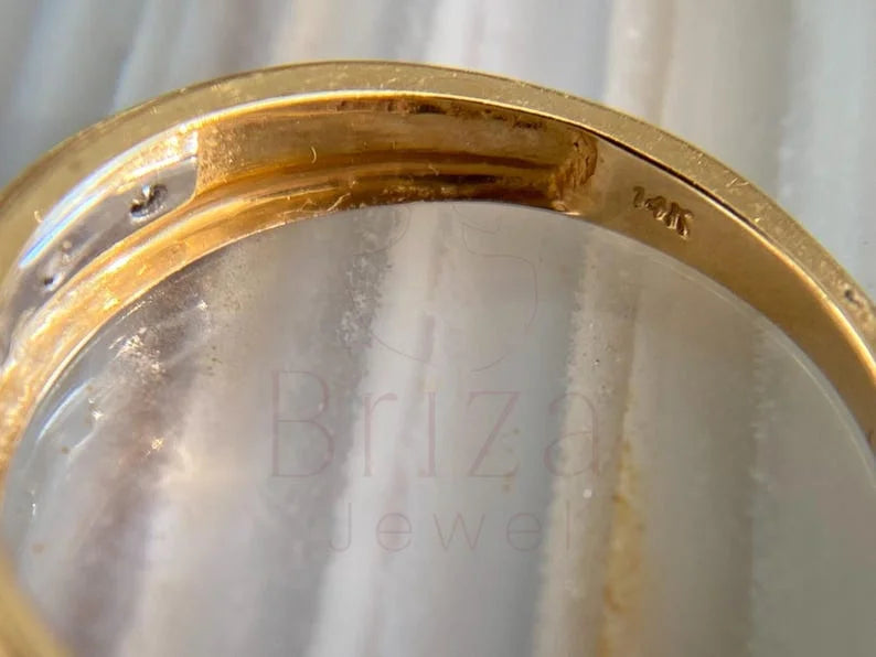 Close-up of a gold ring band with a clear gemstone, showing a 14K stamp on the inner band and a faint 'Briza Jewel' watermark overlay.