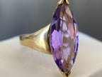 Gold ring with a marquise-shaped purple gemstone on a blurred background